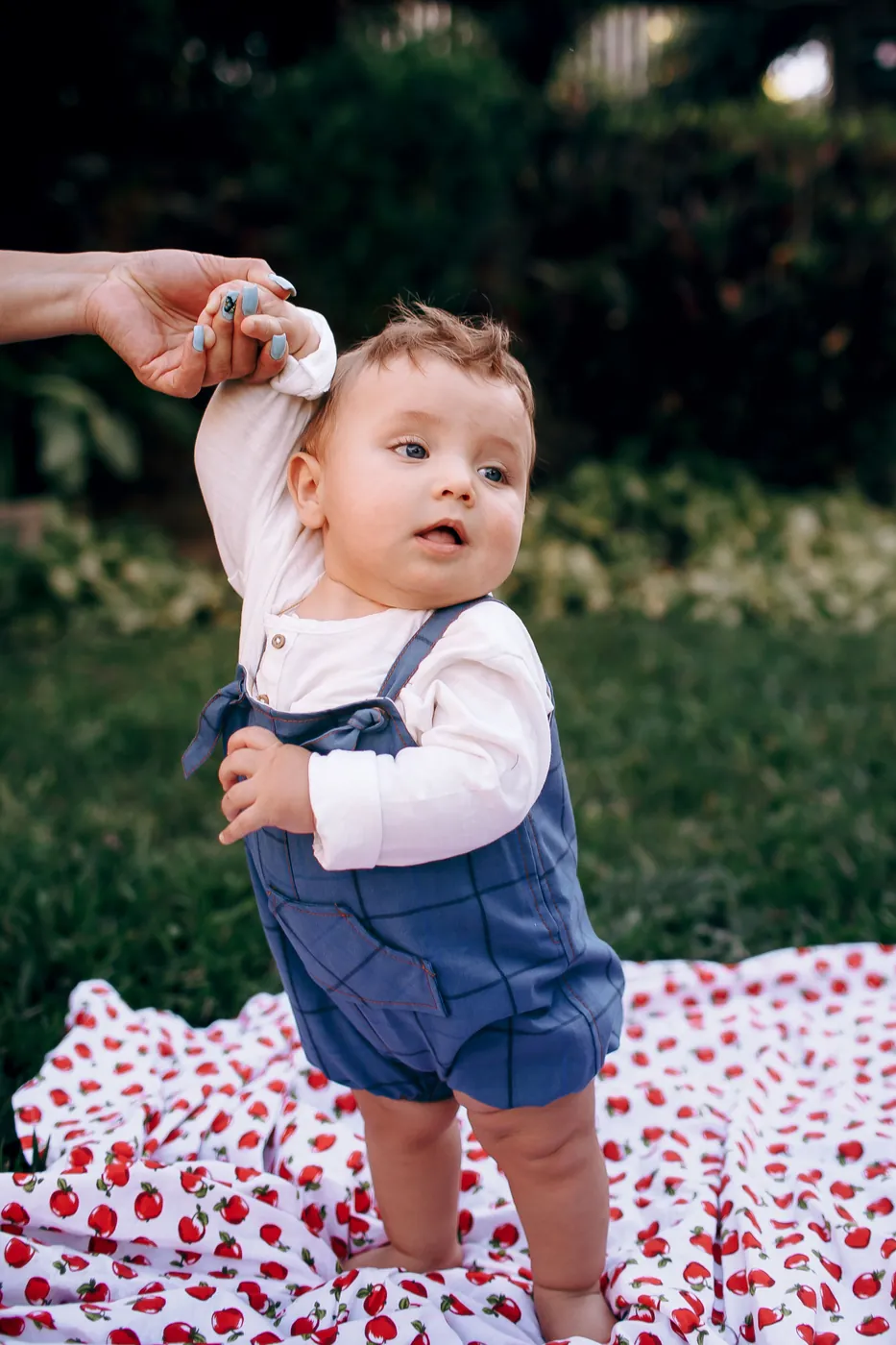 A baby standing up while holding a grown-up's hand