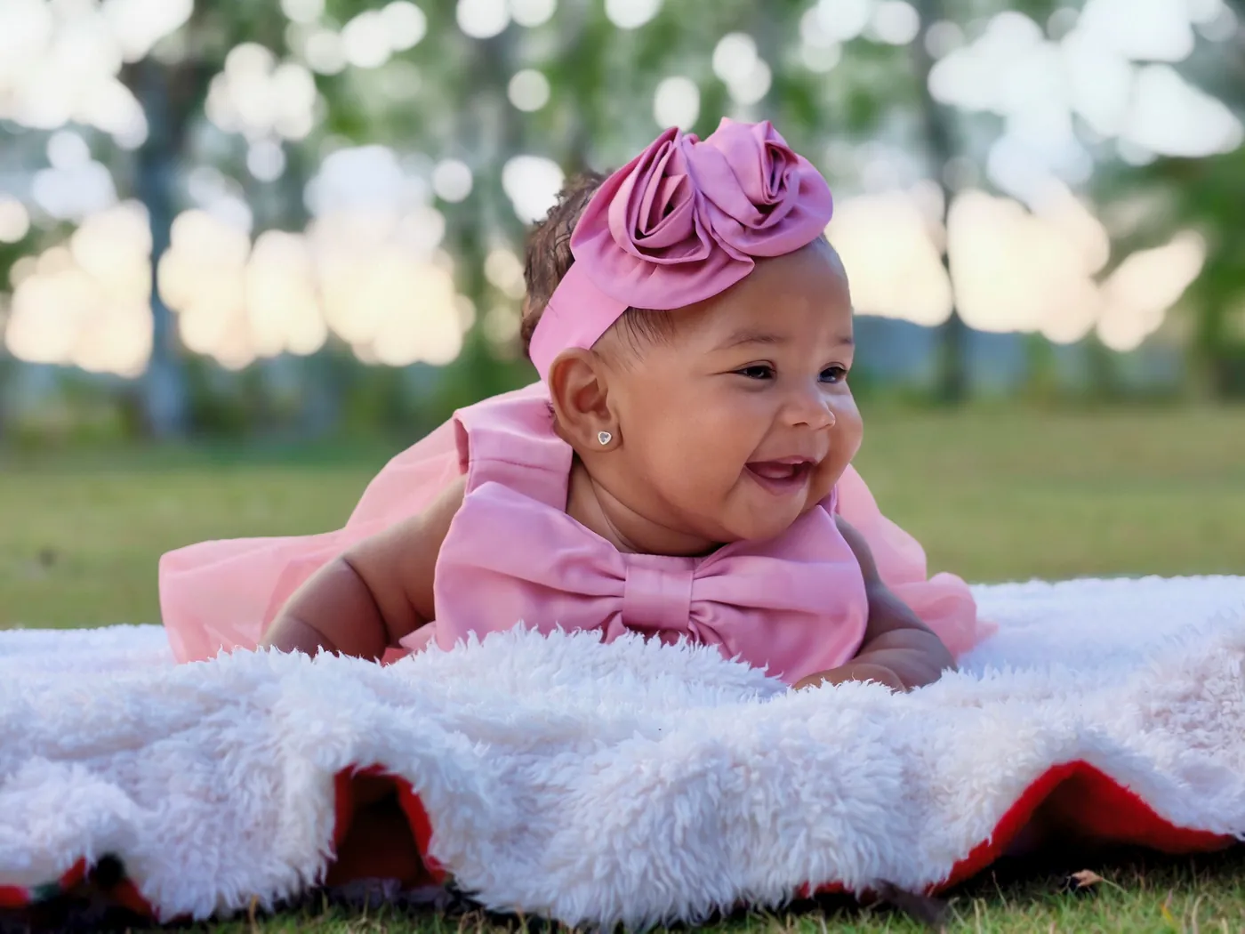 A smiling baby girl in a pink dress lying on a soft blanket